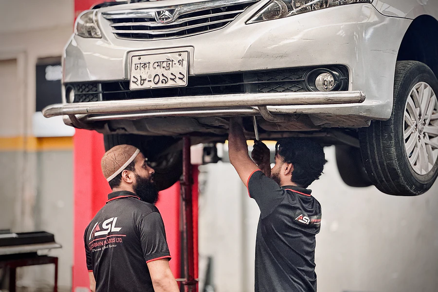 Two Autobahn Solutions technicians inspecting the underside of a car raised on a lift